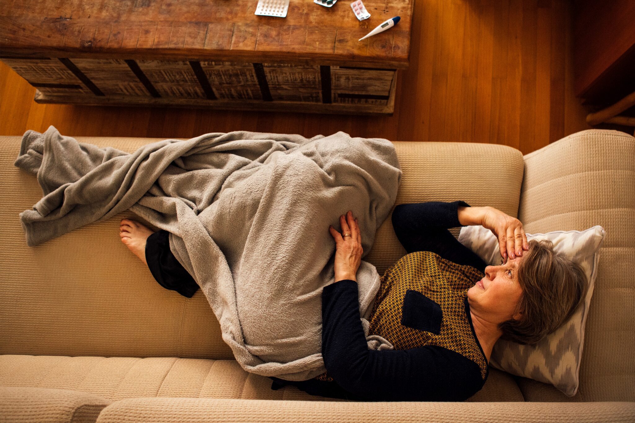 Exhausted teenager resting under a blanket on a sofa in daylight with a hand at the throat, showing the first symptoms of mono
